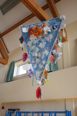 Driffield Infants School Water lantern felt rain drops hang by springs from a sky with sunny face peeping behind fluffy clouds.